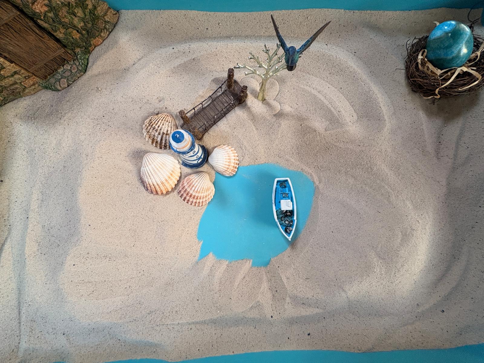 A lighthouse, bridge and shells arranged in a sandtray scene