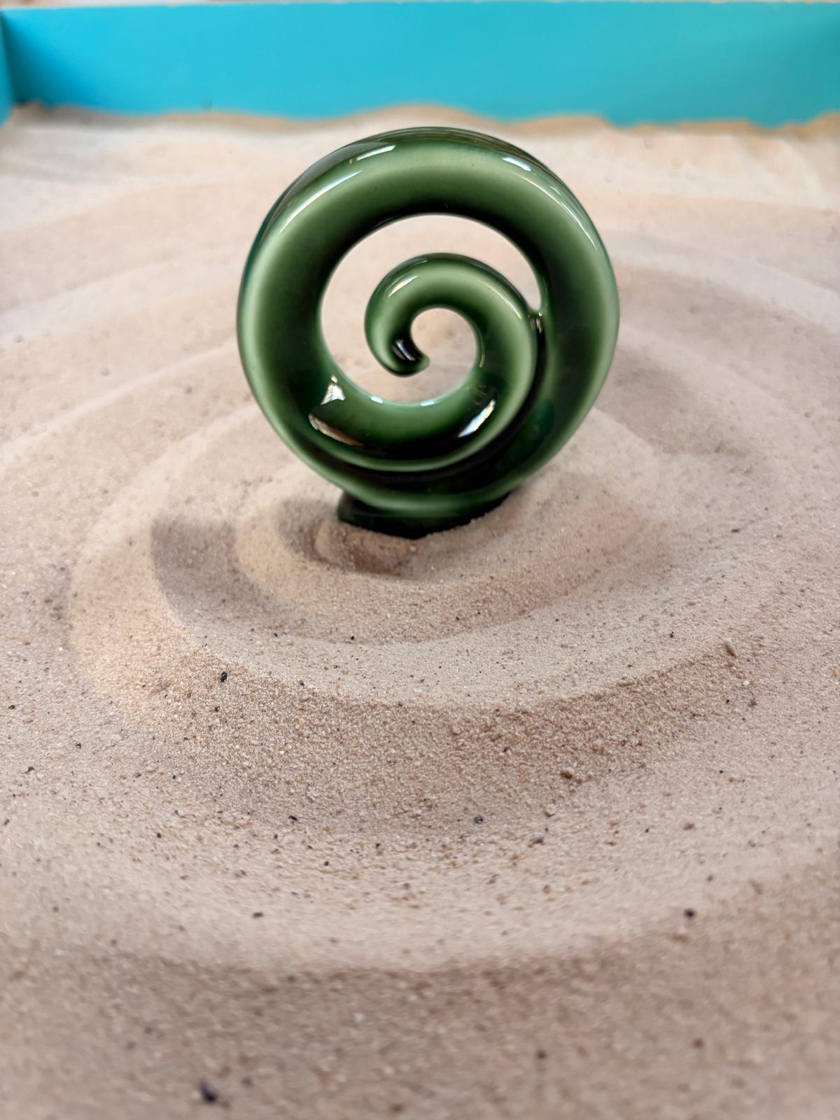 A green spiral ornament resting on raked sand